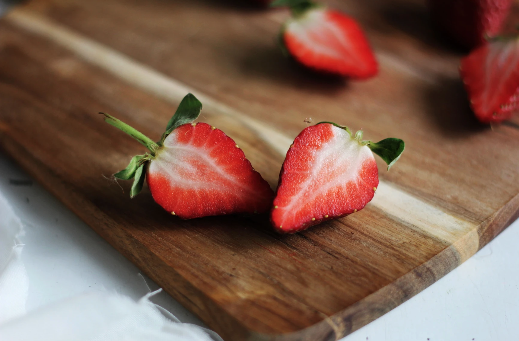 3 strawberries cut in half on a wooden chopping board