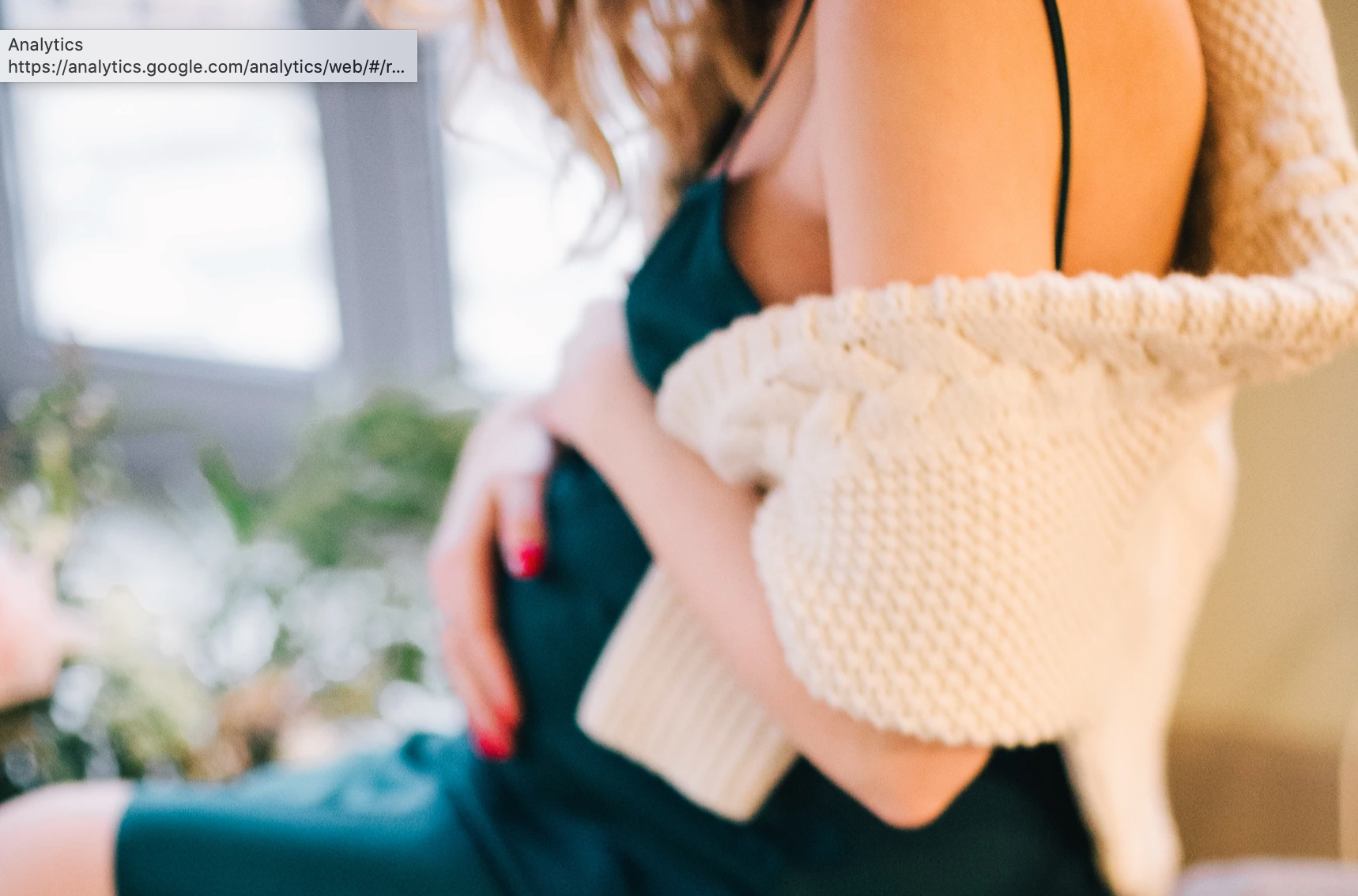 Pregnant woman holding belly wit ha wooly jumper over her shoulders