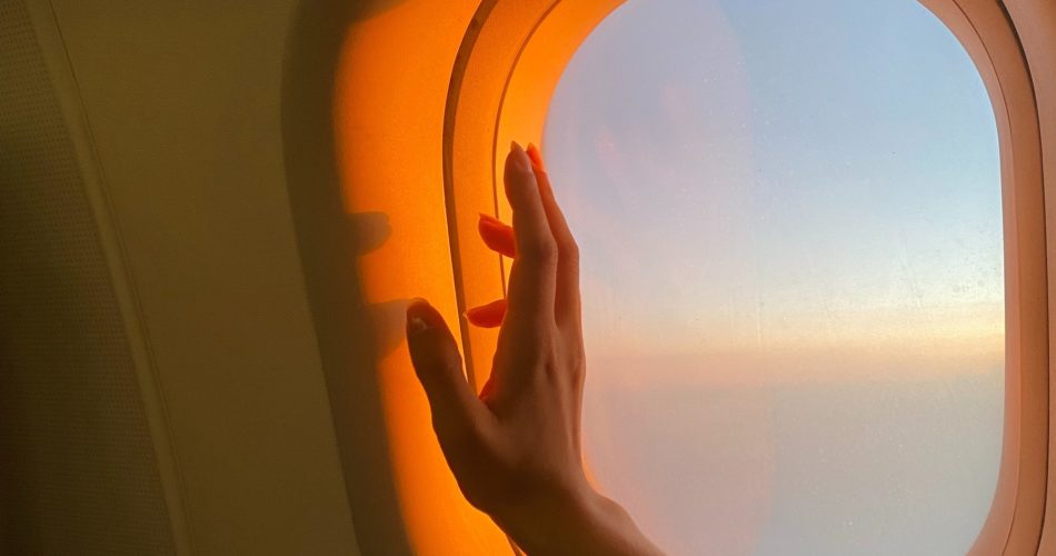 A woman holds her hand up to a plane window with sunlight